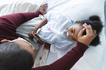 African american girl patient lying on bed with oxygen mask, with her mother at hospital