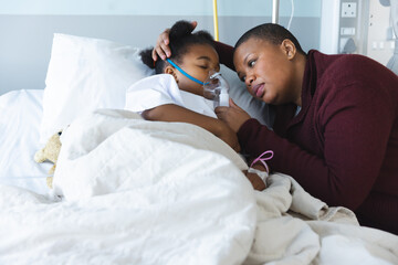 African american girl patient lying on bed with oxygen mask, with her mother at hospital