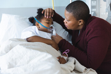African american girl patient lying on bed with oxygen mask, with her mother at hospital