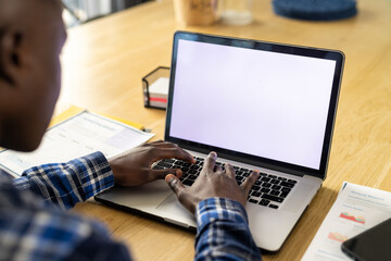 African american man sitting at table, using laptop with copy space on screen at home