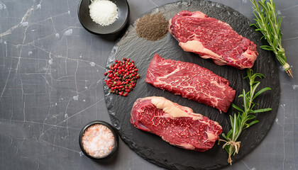 uncooked beef steaks with rosemary and finely ground black peppercorn on a black stone plate, landscape view from above