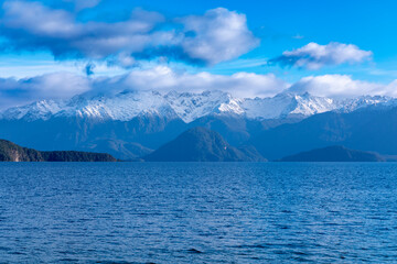 Photograph of a large blue lake and snow-capped mountain range while driving from Te Anau in Fiordland to Manapouri on the South Island of New Zealand