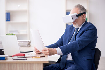 Naklejka premium Old male employee wearing virtual glasses at workplace