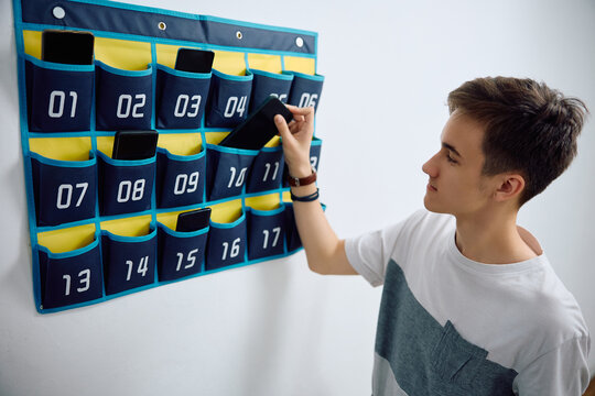 High school student leaves his smart phone in cell phone organizer on wall before entering in classroom at school.