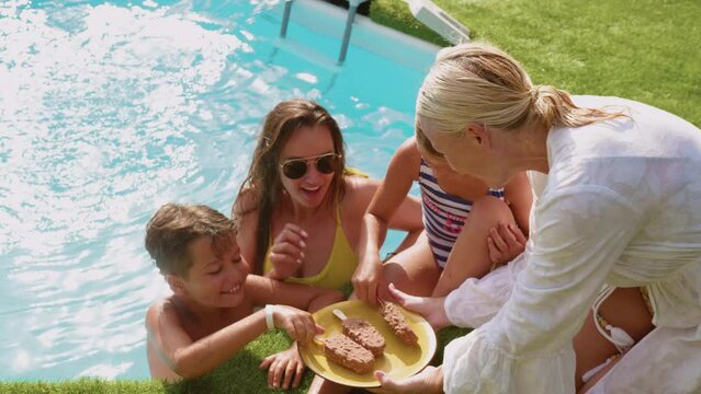 Happy grandmother brings ice cream to her grandchildren and adult daughter in the pool, joint family enjoyment on summer vacation in the pool