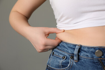 Overweight woman in tight tshirt and jeans on grey background, closeup