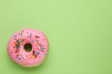 Tasty glazed donut decorated with sprinkles on green background, top view. Space for text