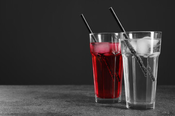 Glasses of different refreshing soda water with ice cubes and straws on grey table, space for text