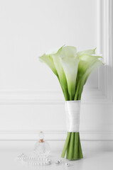 Beautiful calla lily flowers in glass vase, bottle of perfume and jewelry on white table
