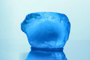 Crystal clear ice cube on light blue background, closeup. Color tone effect