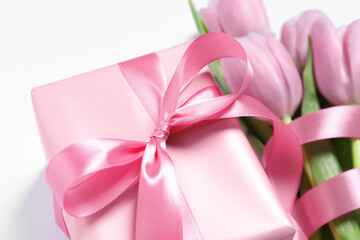 Beautiful gift box with pink bow and tulips on white background, closeup