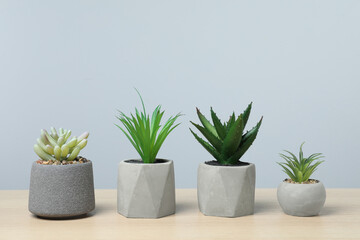 Many different artificial plants in flower pots on wooden table against light grey background