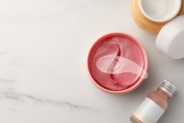 Jar of under eye patches with spoon and cosmetic products on white marble table, flat lay. Space for text