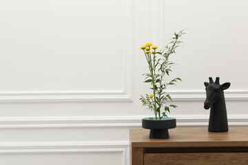 Stylish ikebana with beautiful yellow flowers, green branch and decor carrying cozy atmosphere at home, space for text