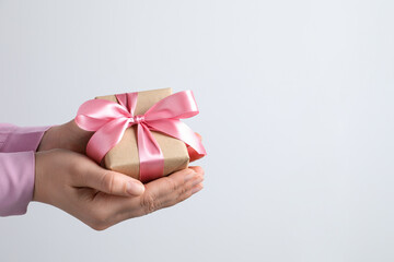 Woman holding gift box with pink bow near white wall, closeup. Space for text