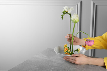 Stylish ikebana as house decor. Woman creating floral composition with fresh flowers at grey table...