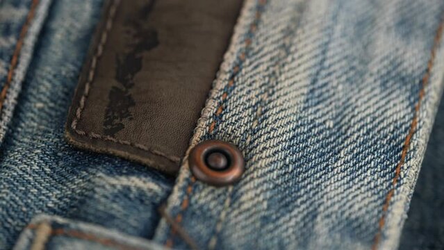rotating the fabric of blue jeans in closeup details. rivet and decorative patch made of genuine leather on the pocket of denim trousers. denim texture, abstract background.