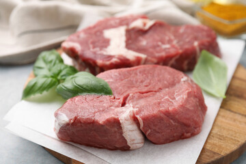 Cut fresh beef meat with basil leaves on wooden board, closeup
