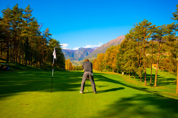 Golfer on Putting Green on Golf Course with Mountain View in Autumn in Lombardy, Italy.