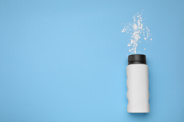 Bottle and scattered dusting powder on light blue background, top view with space for text. Baby cosmetic product