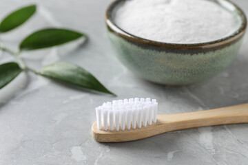 Bamboo toothbrush and bowl of baking soda on light gray marble table, closeup