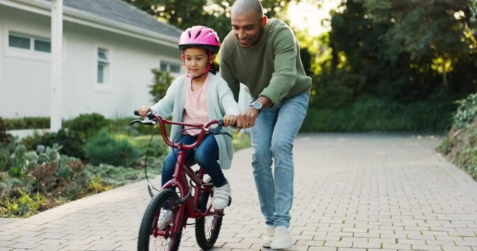 Father helping his kid to ride a bicycle in a green garden on a weekend for a bonding activity. Proud, learning and young dad teaching his daughter cycling on a bike at an outdoor park in nature.