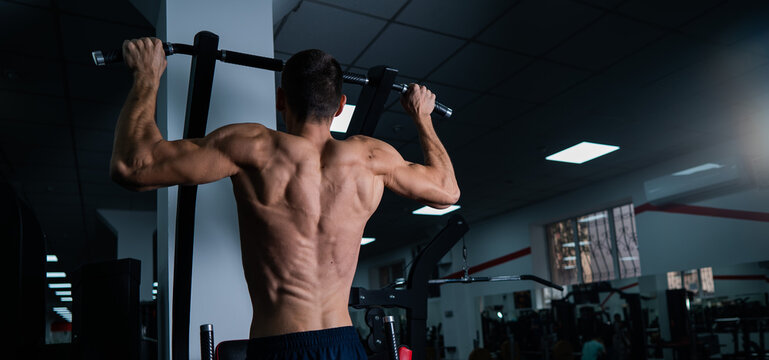 Back view of shirtless man with pull-ups in gym. 