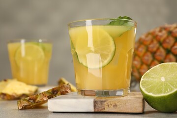 Glasses of tasty pineapple cocktail with mint and lime on light grey table, closeup