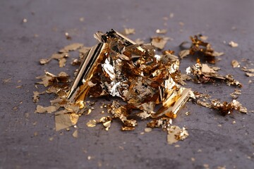 Many pieces of edible gold leaf on grey textured table, closeup