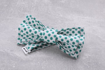 Stylish bow tie with green polka dot pattern on light grey table