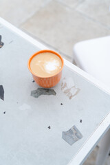 Orange cup with cappuccino on a marble table