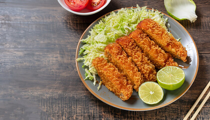 Tonkatsu - panko breaded deep-fried pork cutlet served with fresh shredded cabbage salad, tomatoes and lime slices on a plate, Japanese cuisine, view from above, copy space