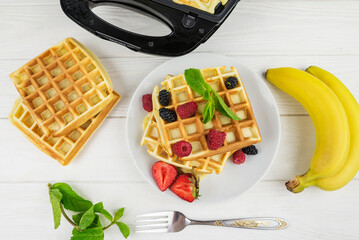 Belgian waffles with different berries on white.