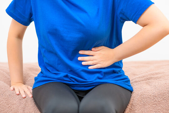 Pacjentka siedząca na ł&oacute;żku, trzymająca się za brzuch