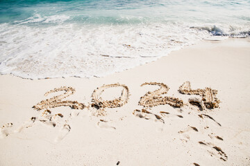 2024 written in white sand on tropical beach, happy New Year