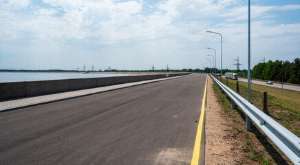 Fototapeta premium Asphalt road next to the concrete bank of the dam