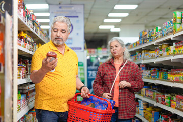 Senior indian couple looking product detail and purchasing together at grocery shop.