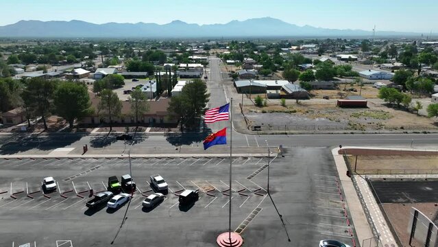 American flag and Arizona state flag waving in parking lot in a small town off of interstate highway. Low income housing in background.
