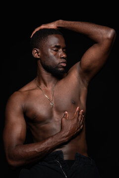 Young black man touching head and showing abs in light