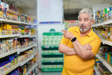 Senior indian man giving expression while purchasing at grocery shop.