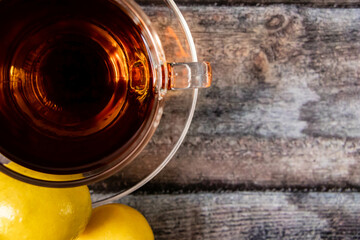 Top close up shot of black tea with lemon on wooden texture.