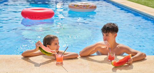Adorable boy and girl eating watermelon and drinking juice on poolside