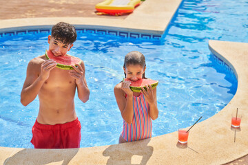 Adorable boy and girl eating watermelon and drinking juice on poolside