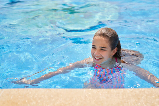 Smiling girl swimming in blue clear pool water