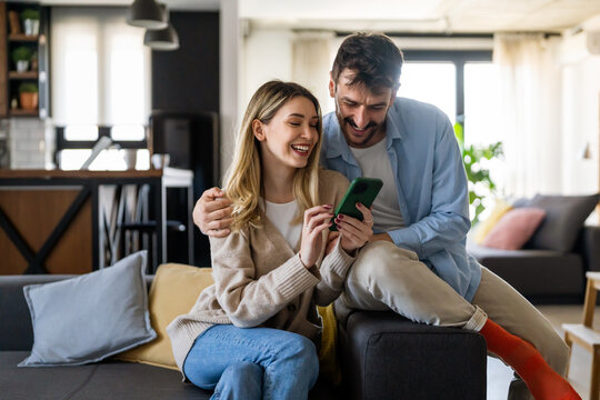 Smiling Young Couple Embracing While Looking At Smartphone. Multiethnic Couple Sharing Social Media