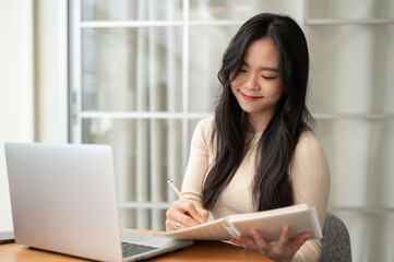 A happy young Asian female college student focuses on studying online at home.