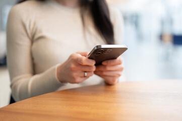 Close-up image of a woman sitting at a table indoors and using her smartphone.