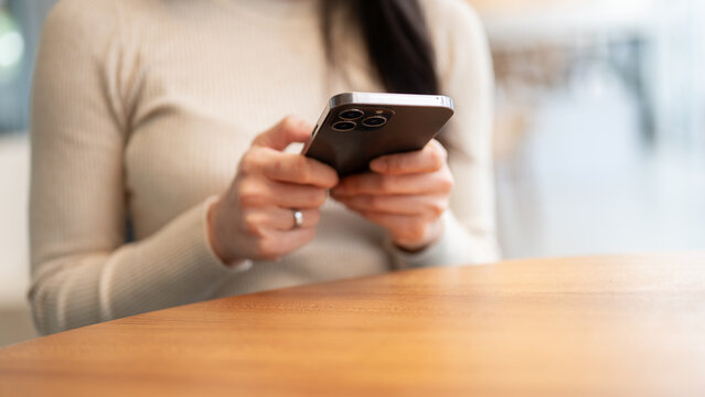 Close-up image of a woman in casual clothes sitting at a table indoors and using her smartphone.