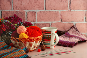 Knitting yarn and a cup of tea on a brick wall background. Balls of yarn in a basket and hot tea create a cozy atmosphere. Knitting is a type of needlework. - Powered by Adobe