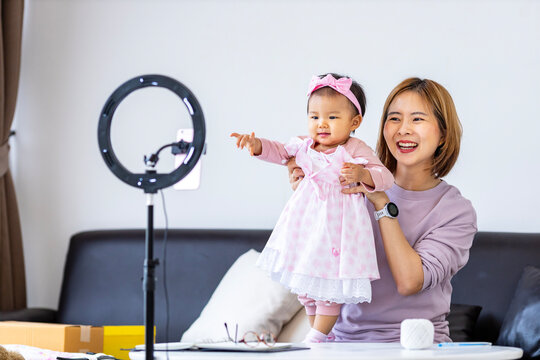 Young Asian influencer mother is selling children clothes live online streaming at home while raising her toddler as the assistance - Powered by Adobe